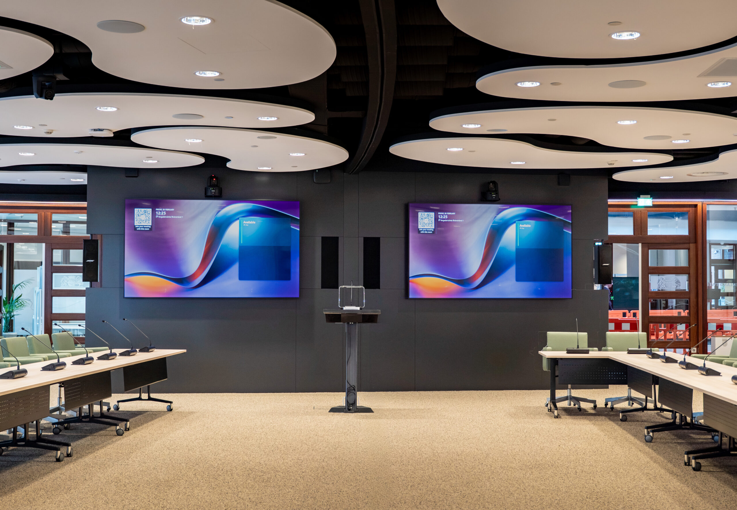 Grote vergaderzaal met twee schermen en een katheder.