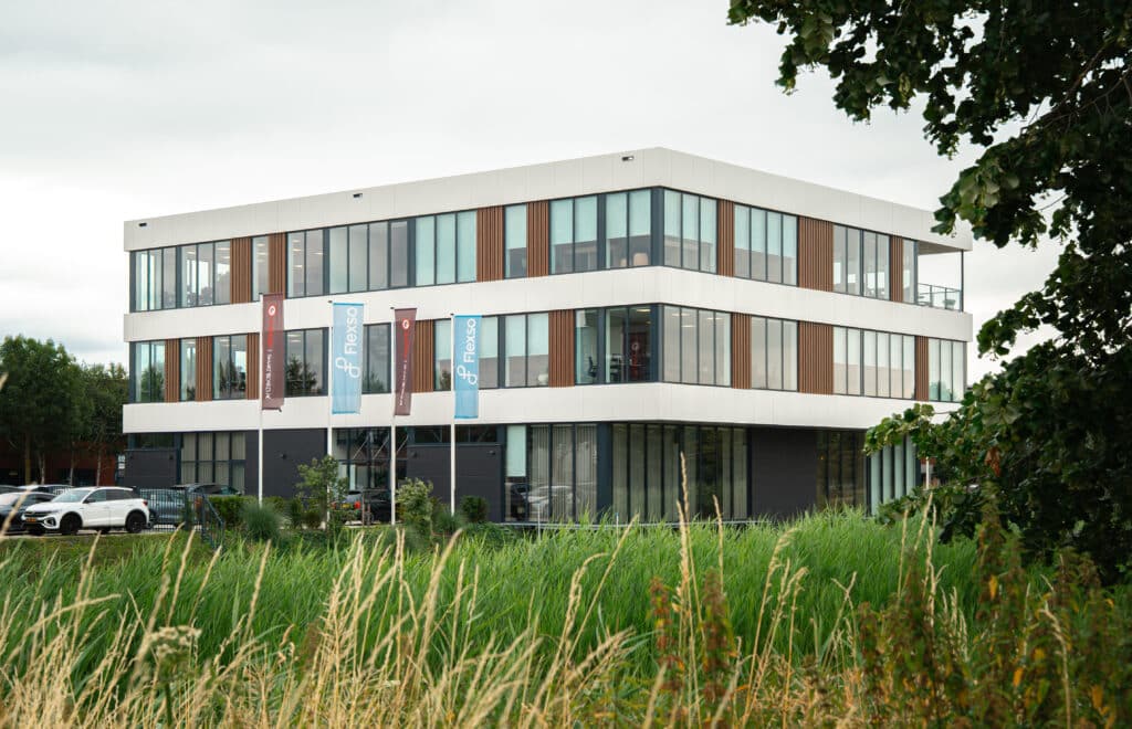 Buitenaanzicht van de showroom in Houten, een modern kantoorgebouw met lichte gevel, houten lamellen en vlaggen van Limid / Smartboard bij de ingang.