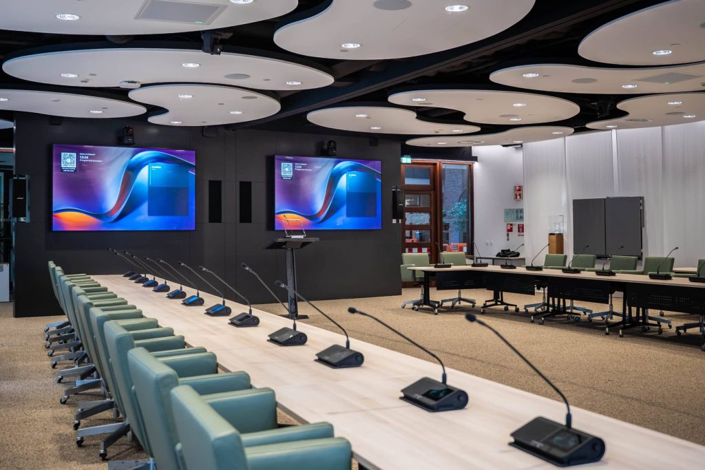 Rivierenzaal met microfoons en schermen.