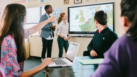 Leerlingen werken samen met elkaar en staan voor een digibord. De school heeft een digibord gekocht. Dit is ook wel een presentatiescherm voor toepassingen in het onderwijs.