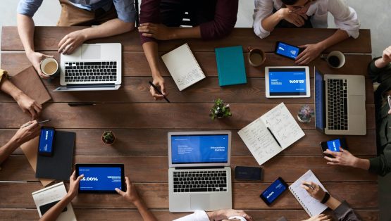 Een team dat aan een houten tafel samenwerkt met verschillende apparaten en notitieblokjes.