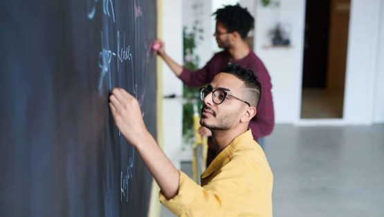 2 personen die iets tekenen op een oud krijtbord. Voor de blog van krijtbord naar interactieve technologie.